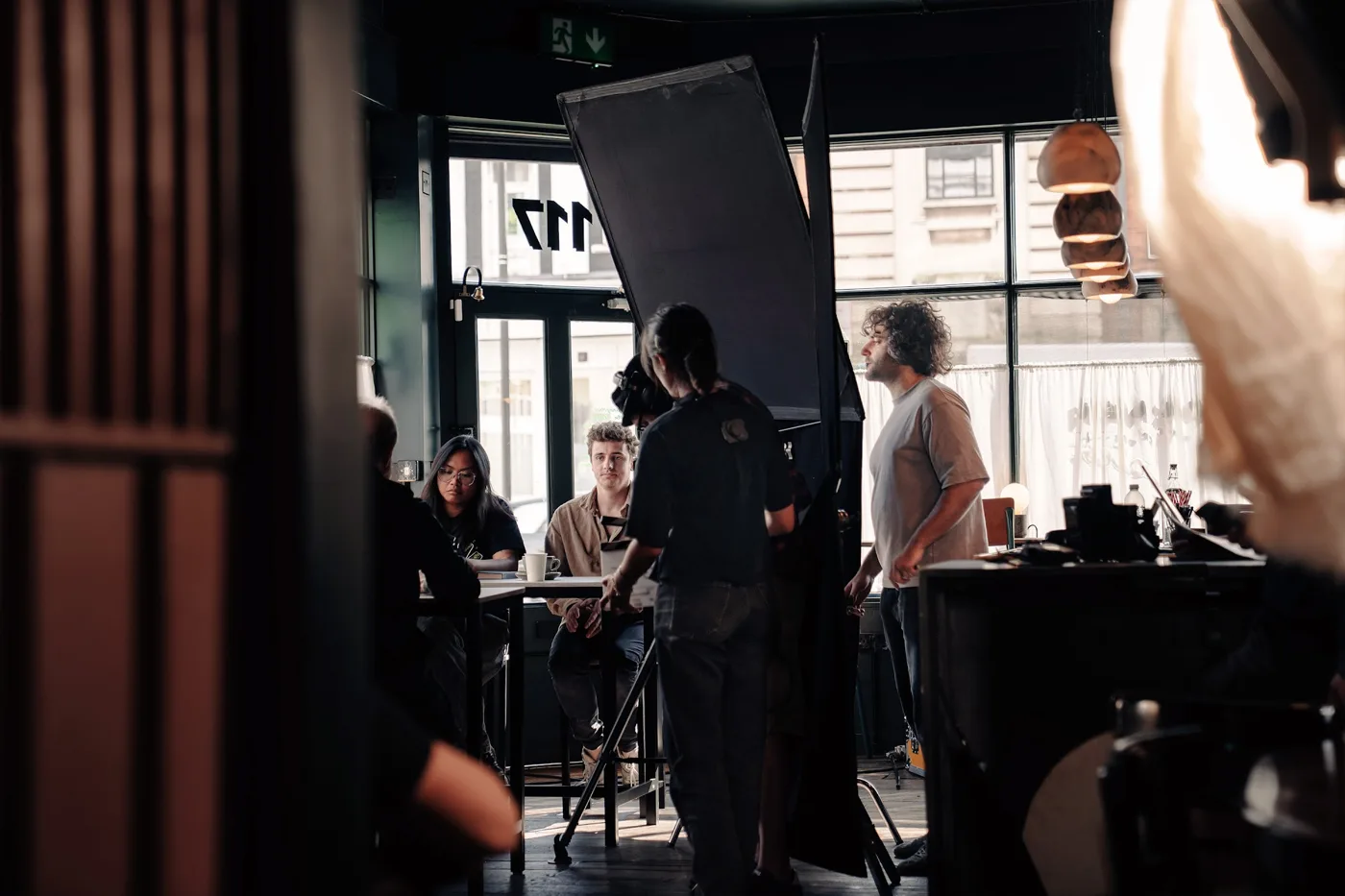 Crew with a large light reflector and camera rig inside a dark cafe