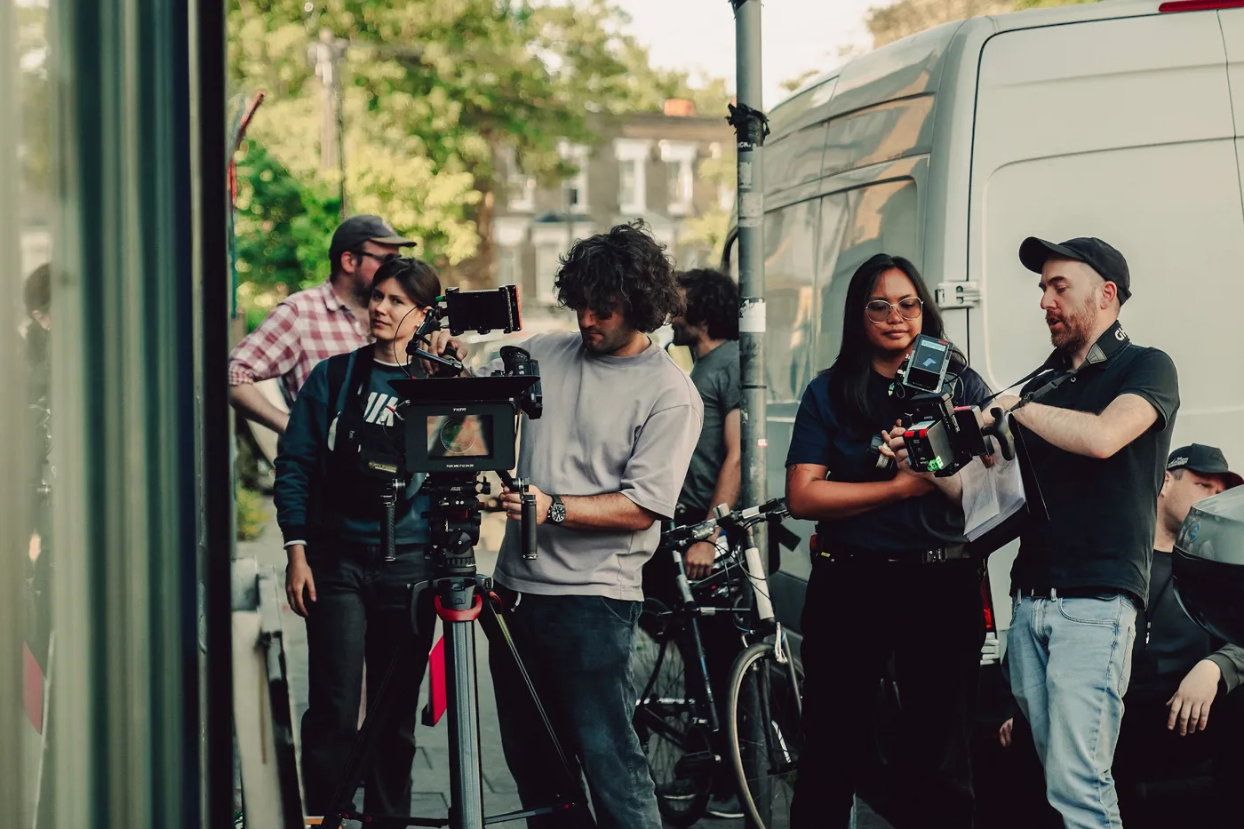 Crew members with a camera on a tripod on the pavement outside, next to a white van