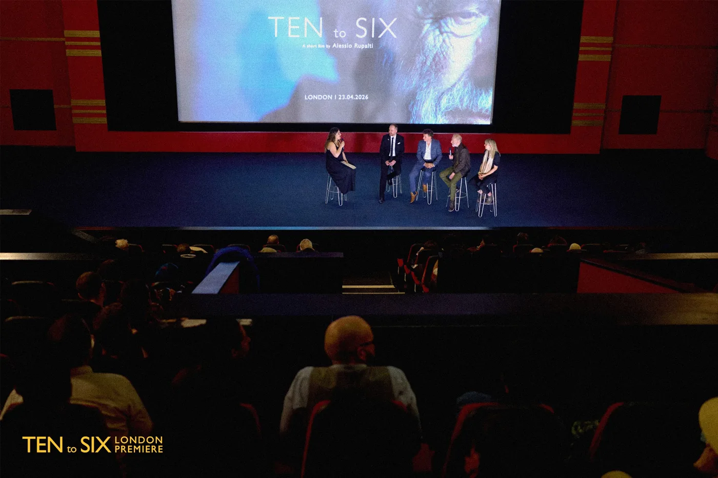 View from the back of a cinema auditorium towards a panel on stage beneath the Ten to Six title