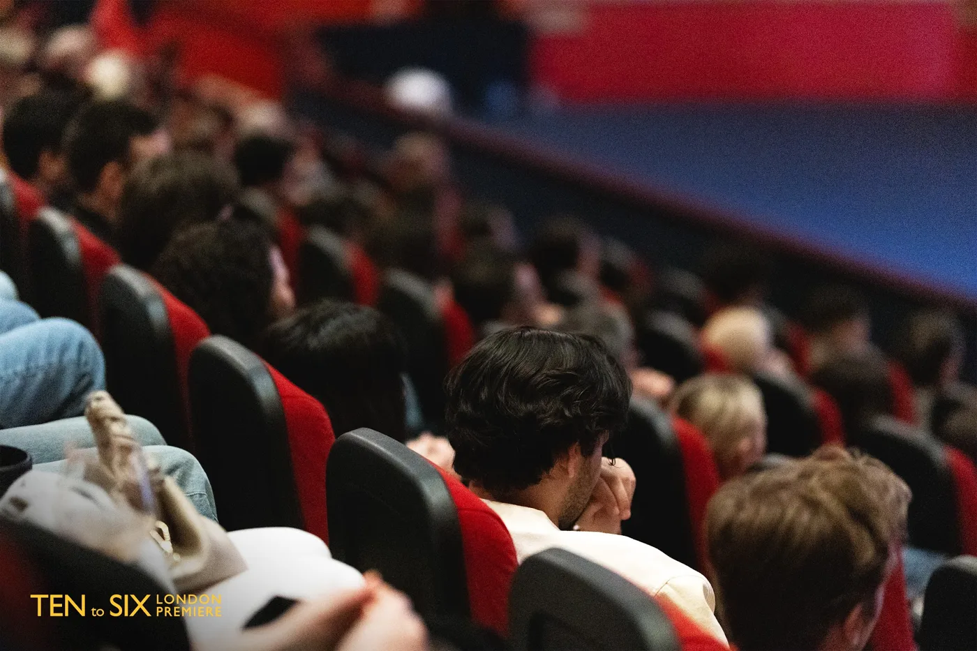 Audience members in red cinema seats, seen from the side