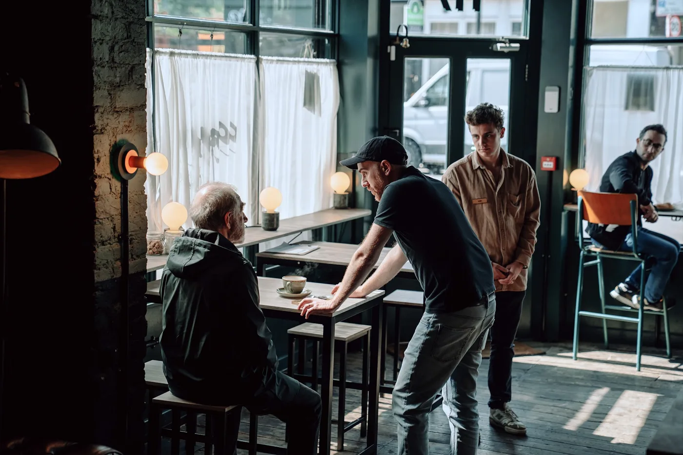 Crew members and actors standing around a high table in a sunlit cafe